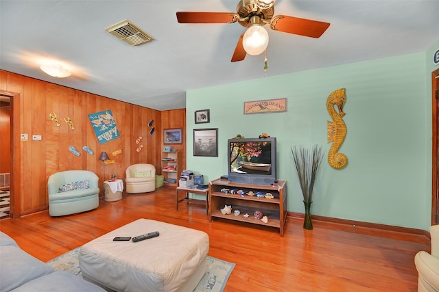 living room with ceiling fan, light hardwood / wood-style floors, and wooden walls