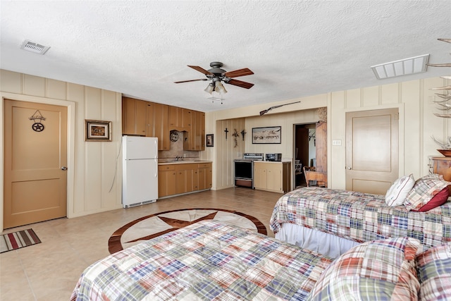 tiled bedroom with sink, ensuite bath, ceiling fan, a textured ceiling, and white fridge