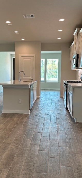 kitchen featuring white cabinets, appliances with stainless steel finishes, a center island with sink, and sink