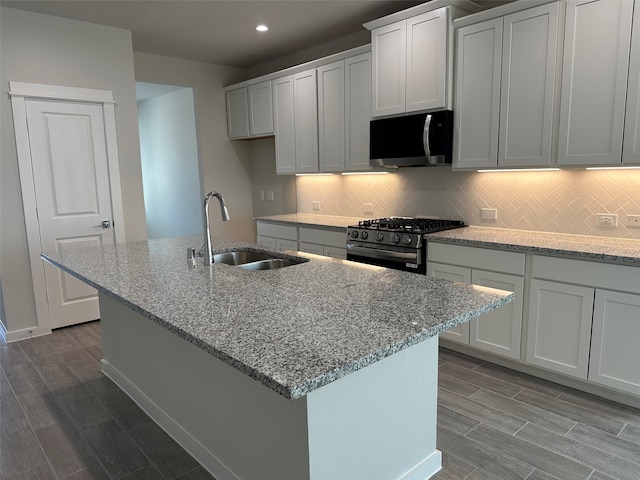 kitchen with sink, range with gas stovetop, light stone countertops, a kitchen island with sink, and white cabinets