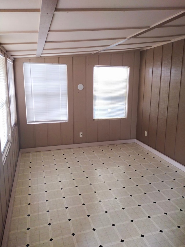 empty room featuring light tile patterned flooring, beamed ceiling, and wood walls