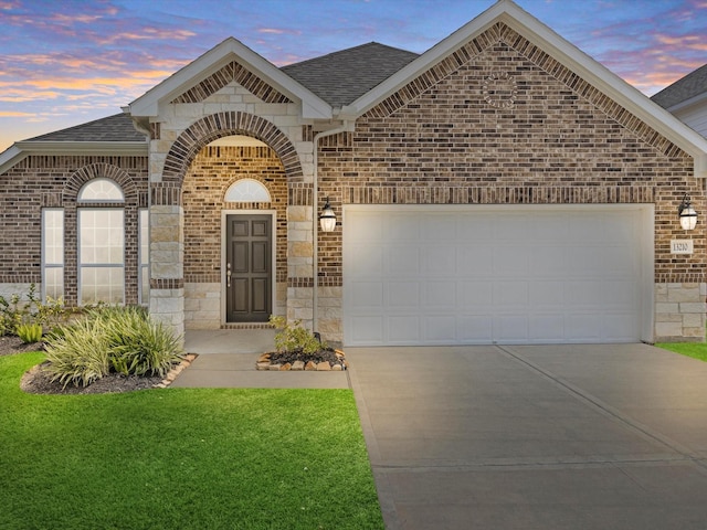 french country inspired facade featuring roof with shingles, brick siding, driveway, and an attached garage