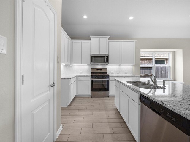 kitchen with light stone countertops, backsplash, appliances with stainless steel finishes, sink, and white cabinets