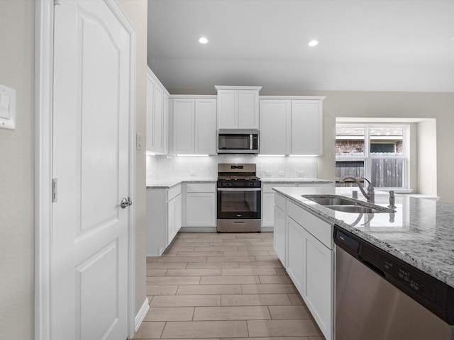 kitchen with backsplash, light stone counters, stainless steel appliances, and a sink