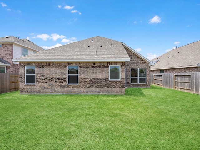 rear view of house featuring roof with shingles, brick siding, a fenced backyard, and a lawn