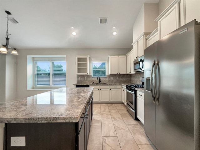 kitchen with decorative light fixtures, white cabinets, appliances with stainless steel finishes, light tile floors, and tasteful backsplash