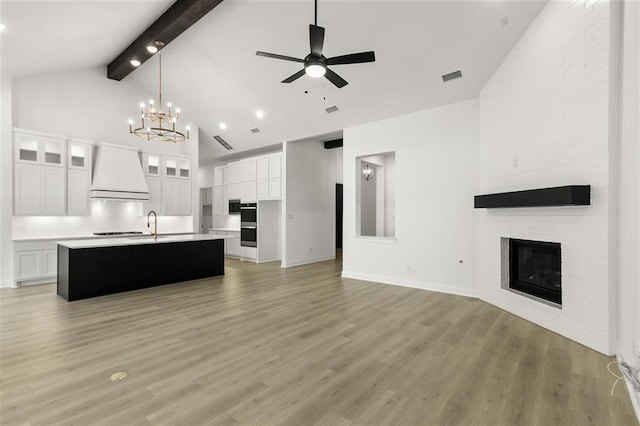 kitchen with white cabinets, premium range hood, light hardwood / wood-style floors, and an island with sink