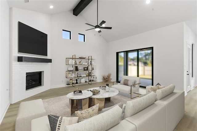 living room featuring high vaulted ceiling, ceiling fan, a fireplace, beamed ceiling, and light hardwood / wood-style floors