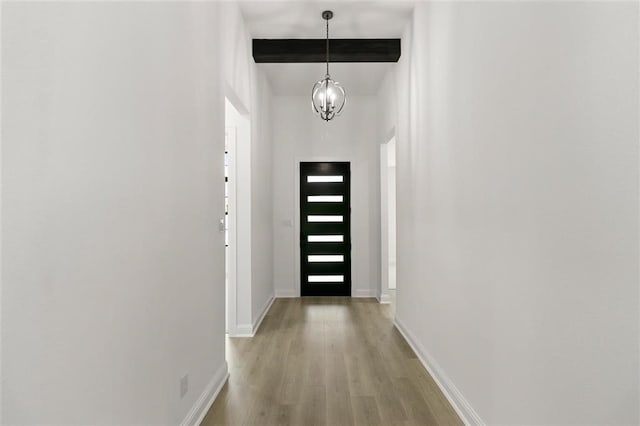 doorway with beam ceiling, light hardwood / wood-style floors, and an inviting chandelier