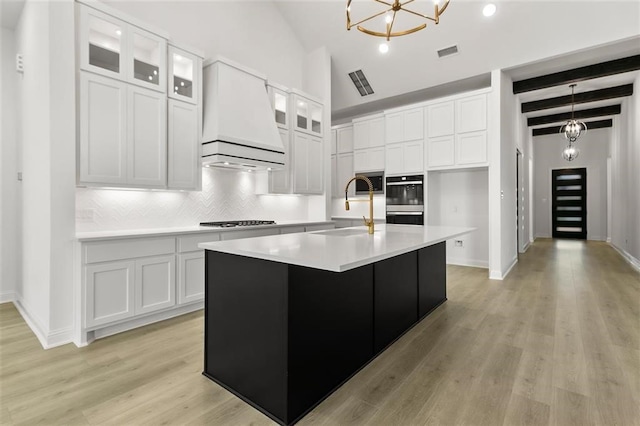 kitchen featuring white cabinets, sink, an island with sink, and a chandelier