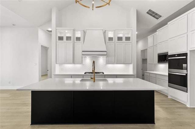 kitchen featuring premium range hood, white cabinets, an island with sink, and stainless steel appliances