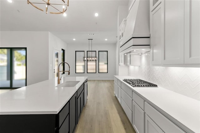 kitchen featuring decorative light fixtures, white cabinetry, a kitchen island with sink, and sink