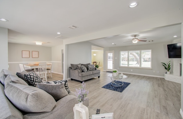 living room featuring ceiling fan, light wood-type flooring, and a brick fireplace