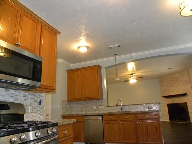 kitchen featuring a large fireplace, stainless steel appliances, visible vents, brown cabinets, and decorative backsplash