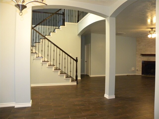 stairway with a large fireplace, ceiling fan, wood finished floors, and baseboards