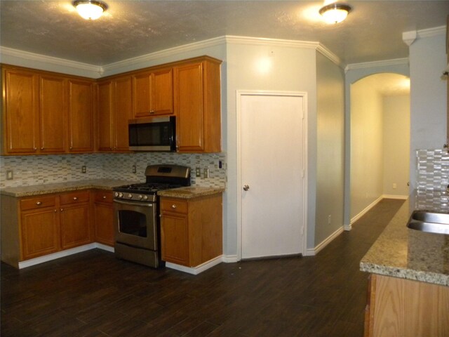 kitchen featuring arched walkways, appliances with stainless steel finishes, dark wood-style floors, and ornamental molding