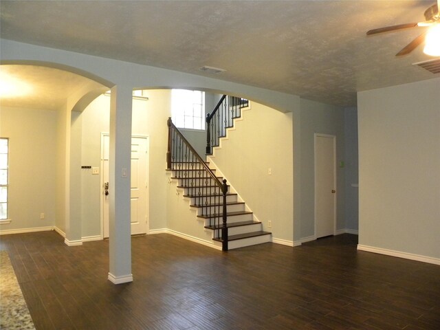 interior space featuring dark wood-type flooring, arched walkways, visible vents, and baseboards