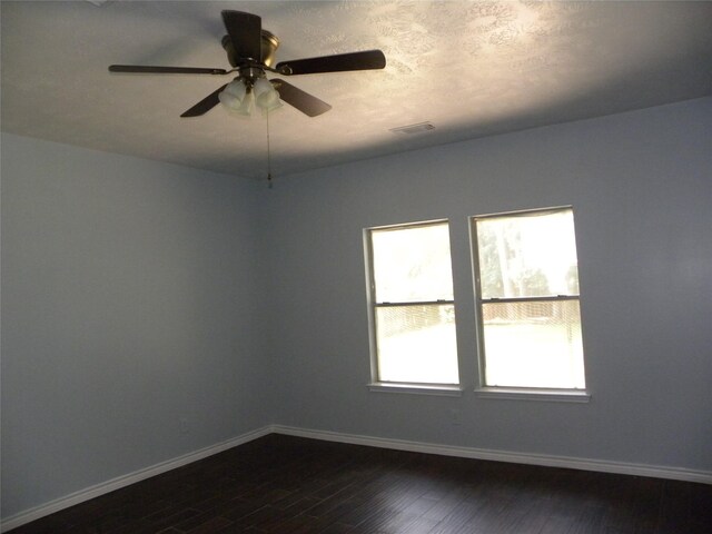 unfurnished room featuring a ceiling fan, visible vents, baseboards, and dark wood-type flooring