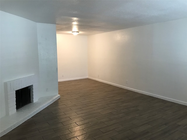 unfurnished living room with a brick fireplace, dark hardwood / wood-style floors, and a textured ceiling