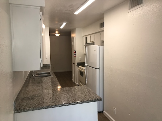 kitchen featuring kitchen peninsula, range with electric stovetop, dark stone counters, sink, and white refrigerator