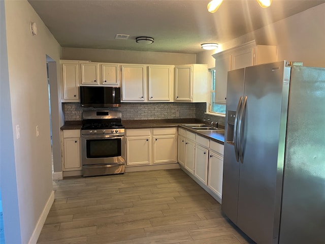 kitchen with white cabinets, backsplash, stainless steel appliances, sink, and light hardwood / wood-style floors