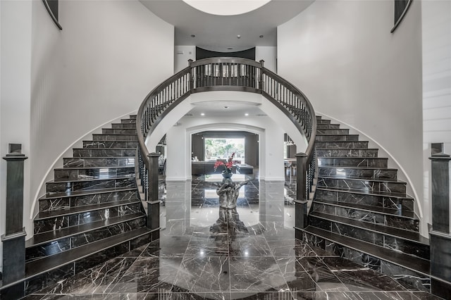 stairway with tile flooring and a towering ceiling