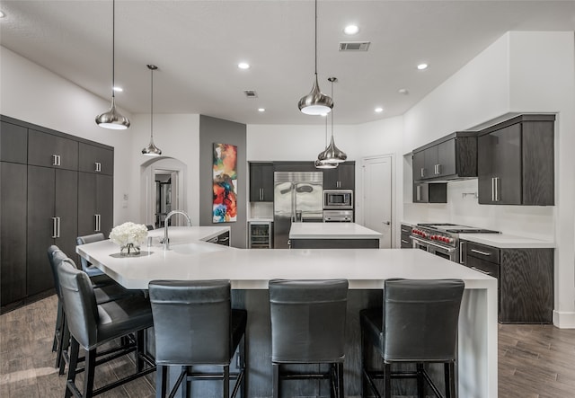 kitchen with sink, a spacious island, dark wood-type flooring, pendant lighting, and built in appliances