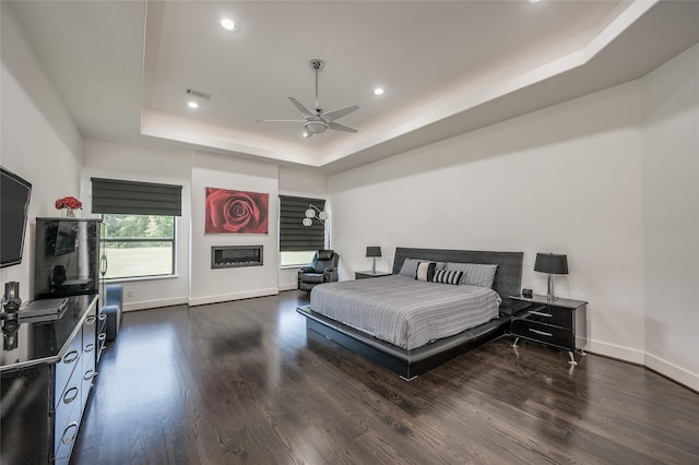 bedroom with ceiling fan, a raised ceiling, and dark wood-type flooring