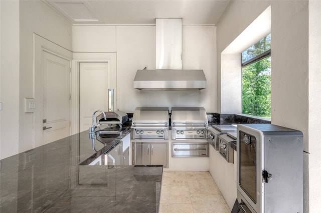 kitchen with wall chimney exhaust hood, fridge, light tile flooring, sink, and dark stone countertops