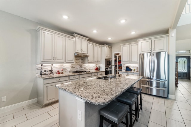 kitchen with an island with sink, sink, a breakfast bar, appliances with stainless steel finishes, and light stone counters