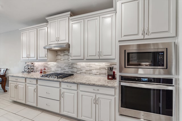 kitchen with white cabinets, stainless steel appliances, light stone counters, and backsplash