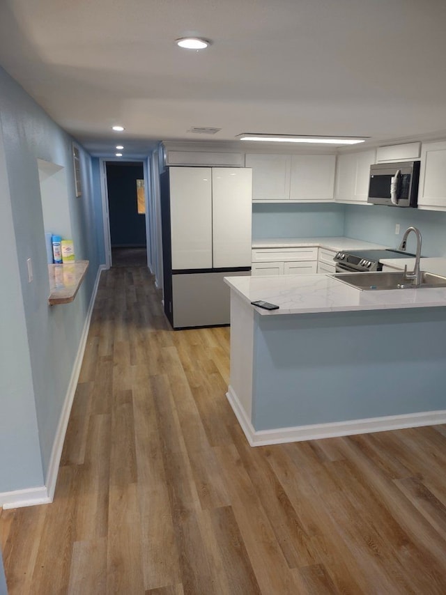 kitchen with white cabinets, stainless steel appliances, kitchen peninsula, and light wood-type flooring