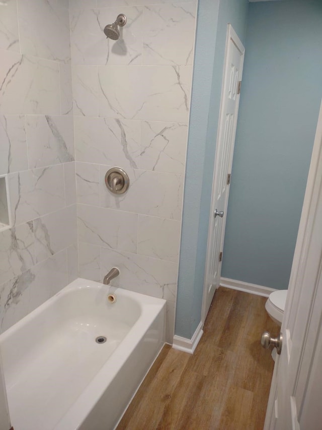 bathroom with hardwood / wood-style floors, tiled shower / bath, and toilet