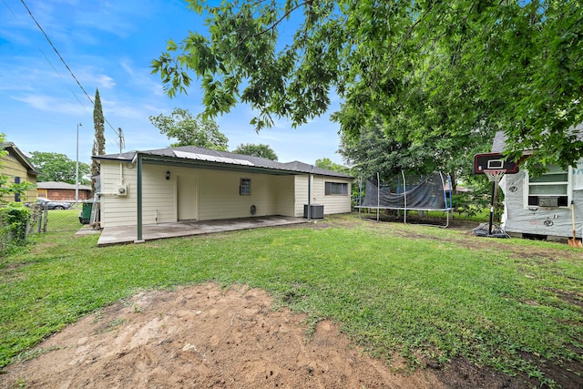 back of house featuring a trampoline, cooling unit, a patio area, and a lawn