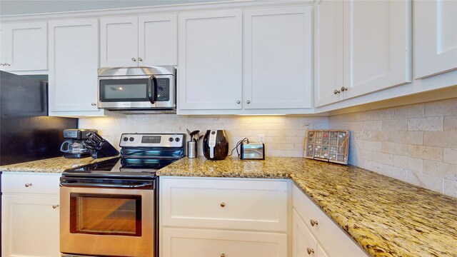 kitchen with appliances with stainless steel finishes, light stone countertops, backsplash, and white cabinetry