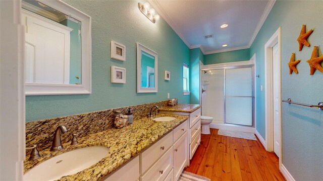 bathroom featuring vanity with extensive cabinet space, toilet, an enclosed shower, double sink, and hardwood / wood-style floors