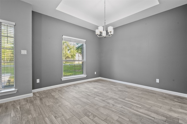 spare room featuring a chandelier, light hardwood / wood-style flooring, and a tray ceiling