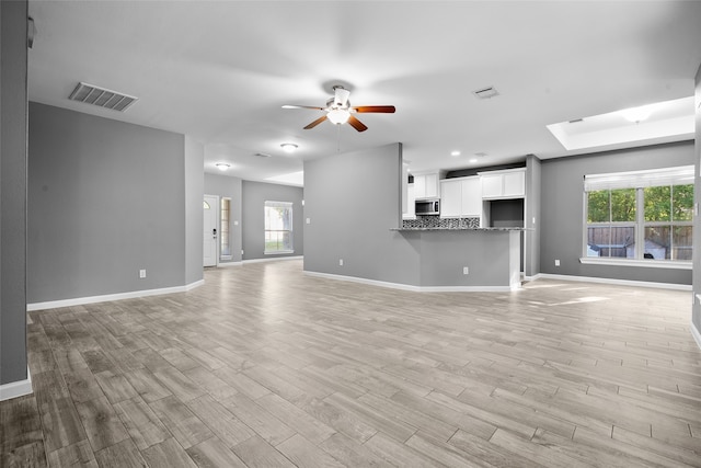 unfurnished living room featuring a skylight, a healthy amount of sunlight, ceiling fan, and light hardwood / wood-style flooring