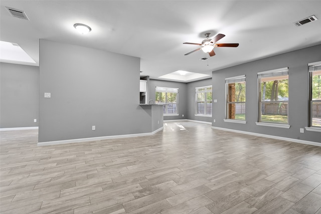 unfurnished living room featuring ceiling fan, a skylight, and light wood-type flooring