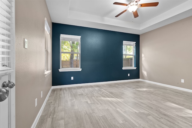 empty room with plenty of natural light, a tray ceiling, and light wood-type flooring