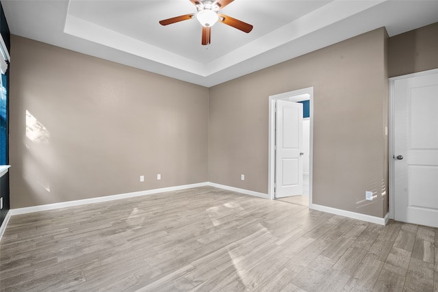 unfurnished room with ceiling fan, a tray ceiling, and light hardwood / wood-style flooring