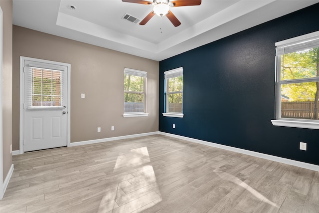 empty room featuring ceiling fan, a wealth of natural light, light wood-type flooring, and a tray ceiling