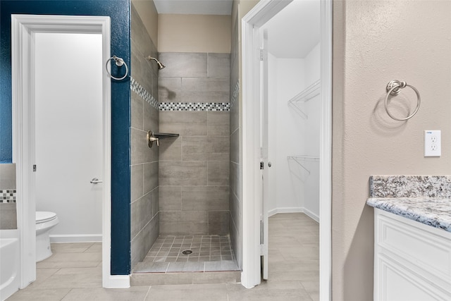 bathroom featuring toilet, tile patterned floors, tiled shower, and vanity