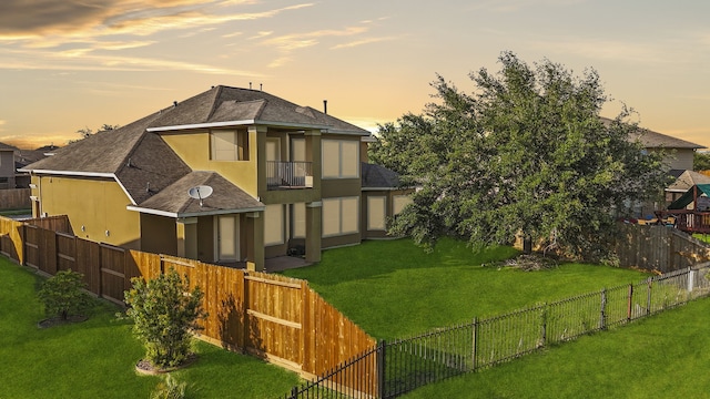 back house at dusk featuring a yard and a balcony