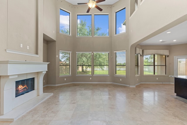 unfurnished living room featuring a wealth of natural light, a towering ceiling, ceiling fan, and light tile floors