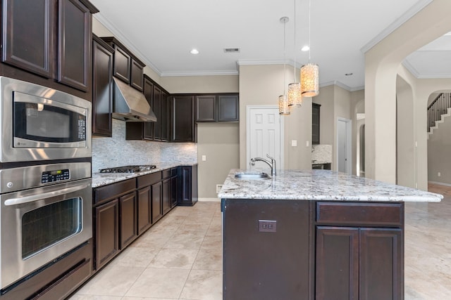 kitchen with backsplash, appliances with stainless steel finishes, wall chimney range hood, and an island with sink