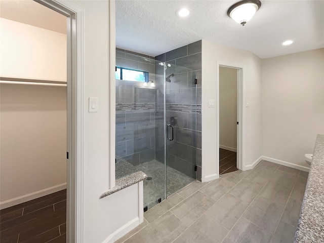 bathroom with toilet, a shower with shower door, and a textured ceiling