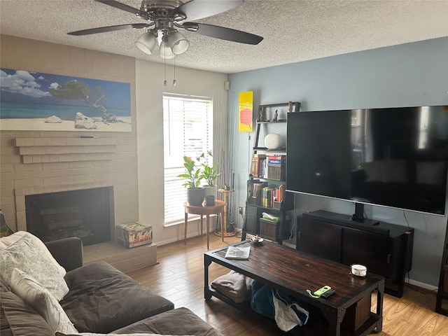 living room with ceiling fan, light wood-type flooring, a fireplace, and a textured ceiling