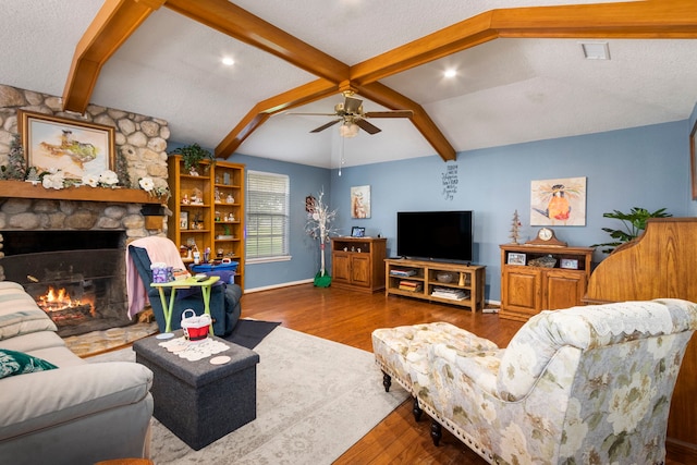 living room featuring lofted ceiling with beams, a fireplace, hardwood / wood-style floors, ceiling fan, and a textured ceiling