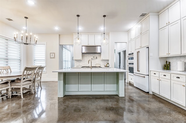 kitchen with high end white fridge, hanging light fixtures, white cabinetry, tasteful backsplash, and an island with sink